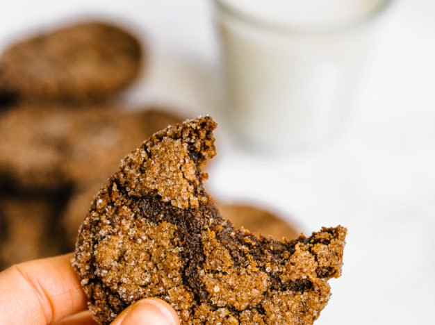 hand holding molasses cookies with bite missing.