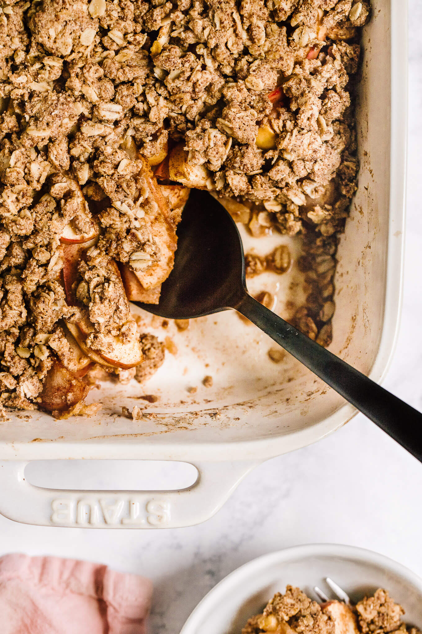 Scooping out a portion of almond butter apple crisp in Stuab baking dish