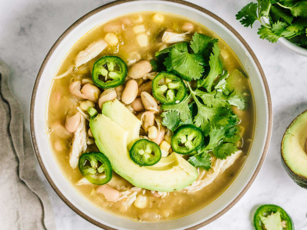 Bowl healthy white chicken chili with avocado slices, jalapenos and cilantro