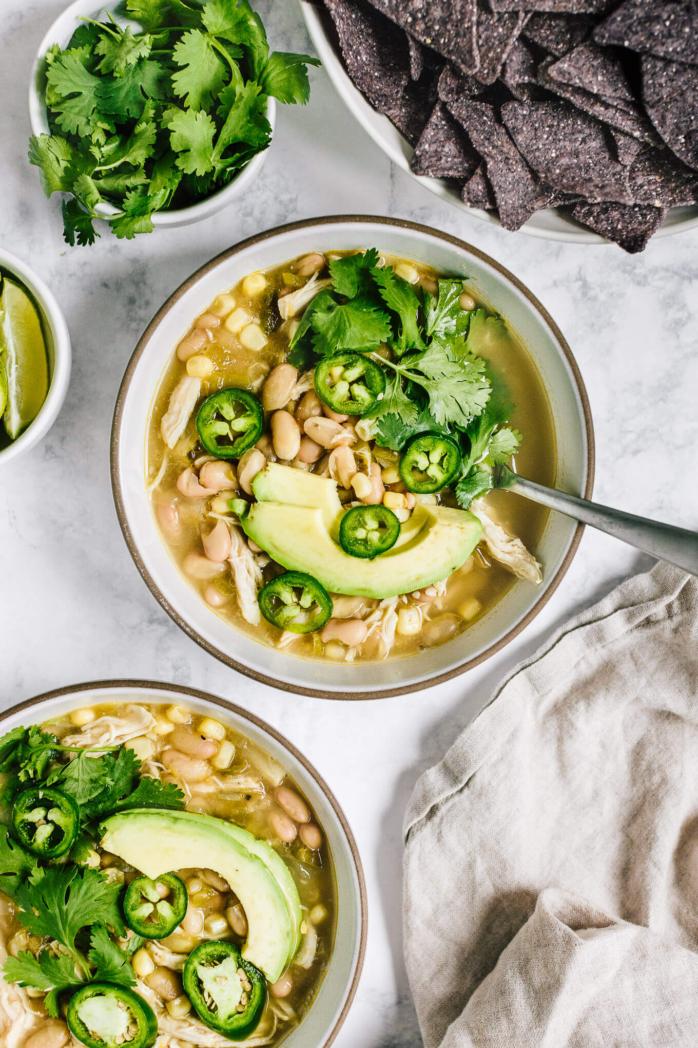 Bowls healthy white chicken chili with avocado slices, jalapenos and cilantro
